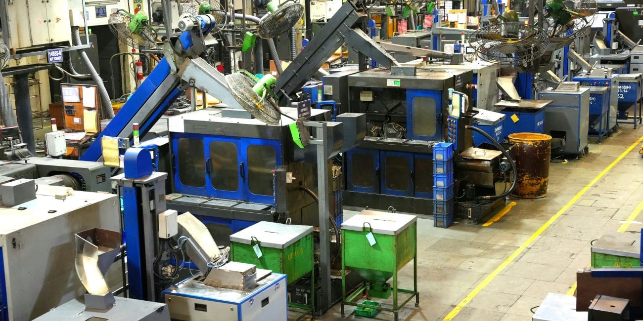 Hakkımızda 2 Toker Sogutma - Aydınlık ve düzenli bir fabrikanın içinde, otomatik makineler ve robot kolların sıralandığı bir ortam; soğutma sistemleri, yeşil çöp kutuları, metal yüzeyler ve tavandan geçen kablolarla bütünleşmiş durumda. Zeminde, geçiş yolları ve güvenlik için sarı çizgiler bulunmakta.